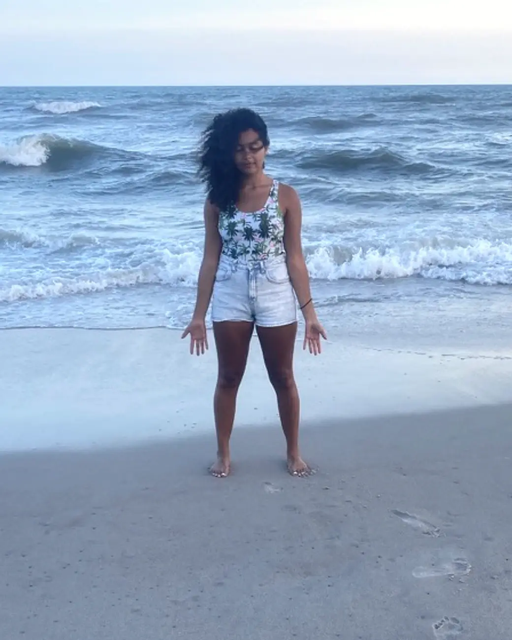 Bri Parks standing barefoot on the beach with ocean waves behind her